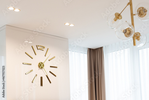 A huge clock in gold color on the wall in a modern beige interior. Interior Design. Soft selective focus, artistic noise.