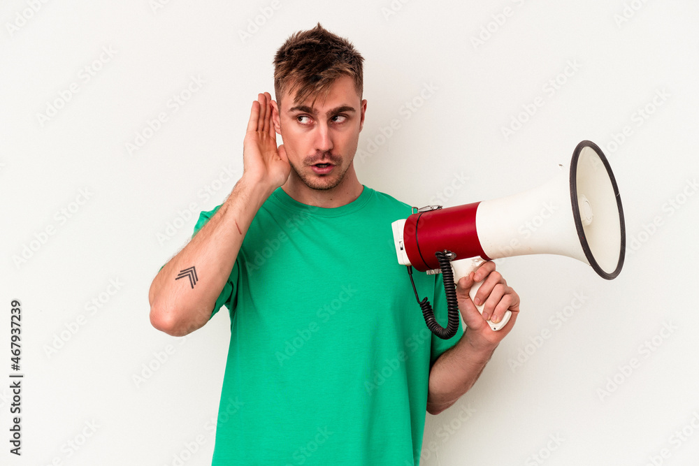 Young caucasian man holding megaphone isolated on white background trying to listening a gossip. Young caucasian man holding megaphone isolated on white background trying to listening a gossip.