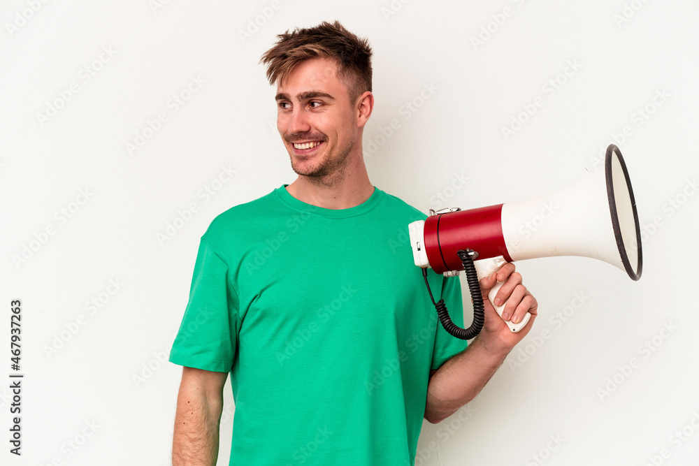 Young caucasian man holding megaphone isolated on white background looks aside smiling, cheerful and pleasant. Young caucasian man holding megaphone isolated on white background looks aside smiling, cheerful and pleasant.
