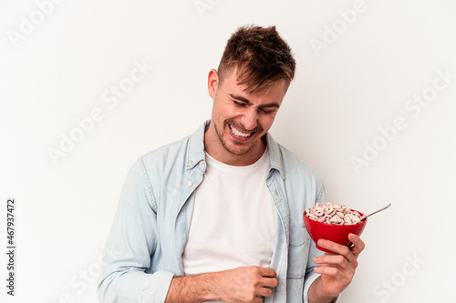 Young caucasian man holding a bowl of cereals isolated on white background laughing and having fun.