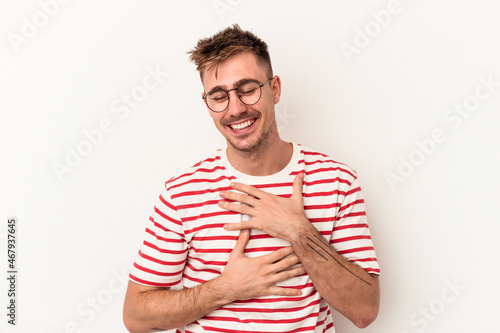 Young caucasian man isolated on white background laughs happily and has fun keeping hands on stomach.