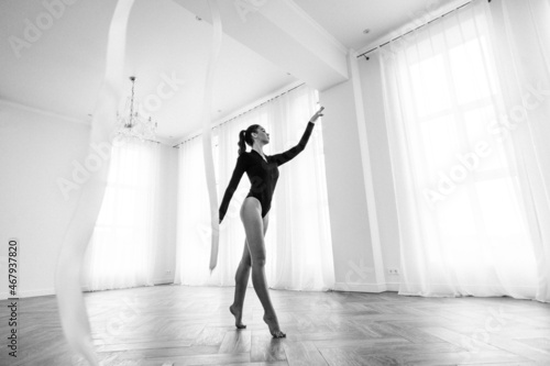girl gymnast  is engaged with gymnastic objects in a light room  she is in a black leotard  performs exercises.