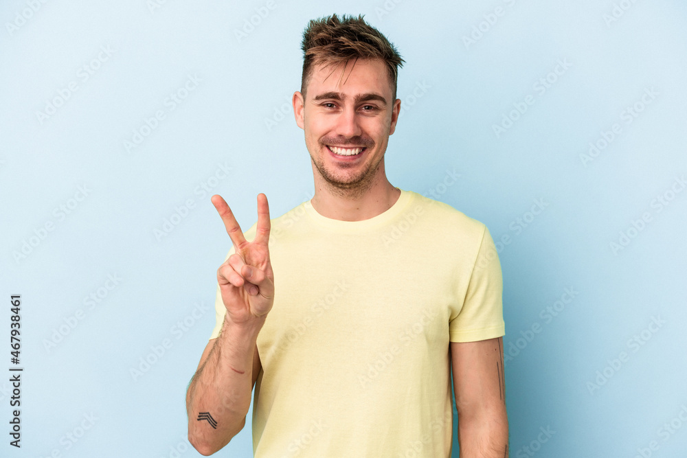 Fototapeta premium Young caucasian man isolated on blue background showing victory sign and smiling broadly.