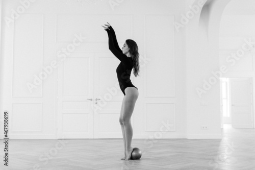 Fototapeta Naklejka Na Ścianę i Meble -  girl gymnast, is engaged with gymnastic objects in a light room, she is in a black leotard, performs exercises.