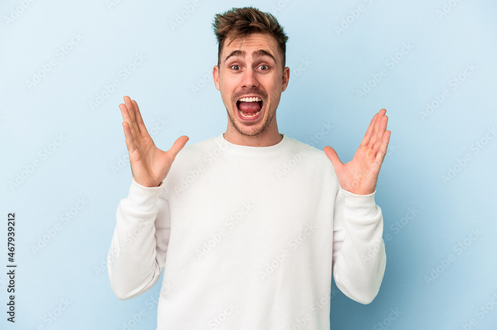 Young caucasian man isolated on blue background receiving a pleasant surprise, excited and raising hands. Young caucasian man isolated on blue background receiving a pleasant surprise, excited and raising hands.