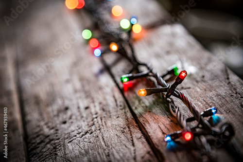 christmas garland of colorful light bulbs on an dark old weathered vintage table or wooden brown board. Christmas decoration, New Years Eve. Selective focus, bokeh, space for text.