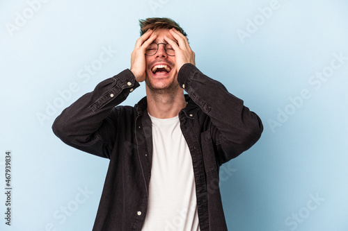 Young caucasian man isolated on blue background laughs joyfully keeping hands on head. Happiness concept.