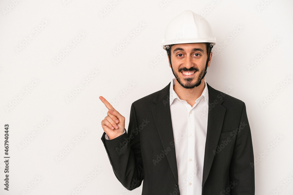 Young architect man wearing a construction helmet isolated on white background smiling and pointing aside, showing something at blank space. Young architect man wearing a construction helmet isolated on white background smiling and pointing aside, showing something at blank space.