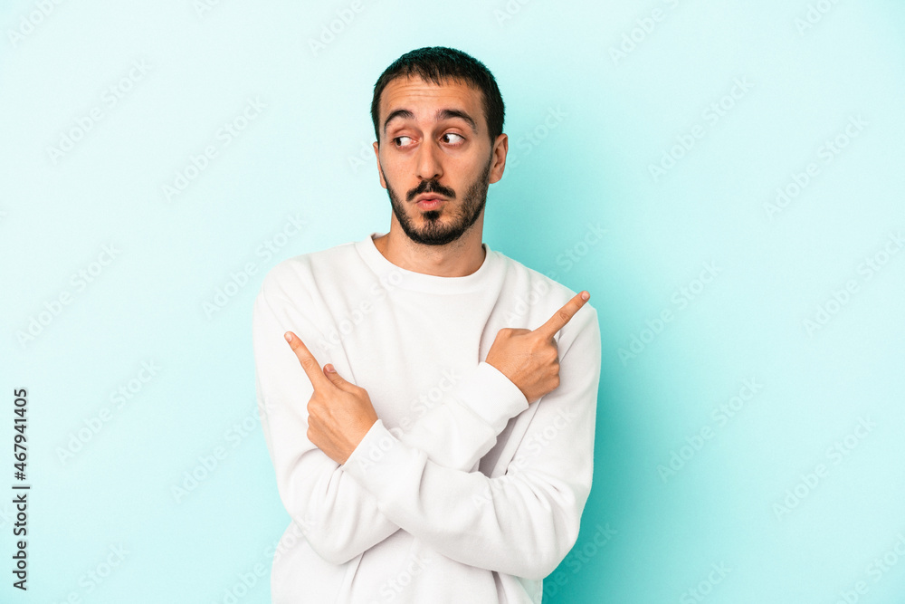 Young caucasian man isolated on blue background points sideways, is trying to choose between two options. Young caucasian man isolated on blue background points sideways, is trying to choose between two options.
