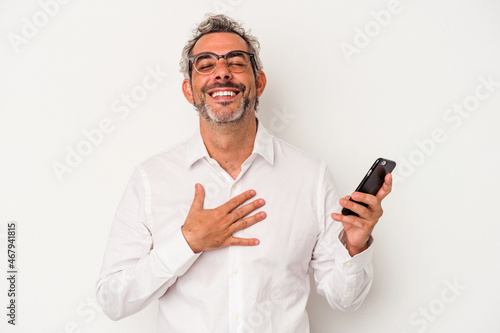 Middle age caucasian business man holding a mobile phone isolated on white background  laughs out loudly keeping hand on chest. © Asier