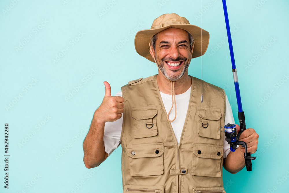 Middle age caucasian fisherman holding rod isolated on blue background smiling and raising thumb up Middle age caucasian fisherman holding rod isolated on blue background smiling and raising thumb up
