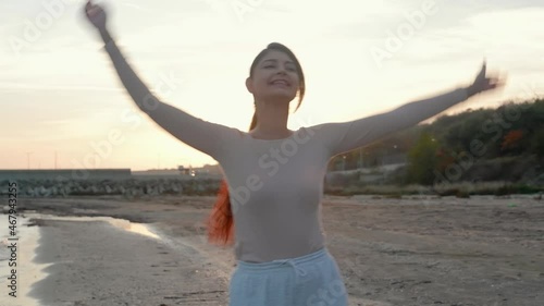 young girl on the beach, dressed, whirling in the rays of the sun raising her hands up