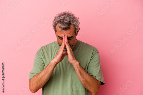 Middle age caucasian man isolated on pink background  praying  showing devotion  religious person looking for divine inspiration.