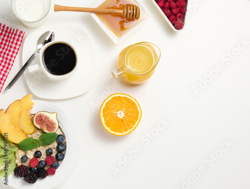 cup of black coffee, a plate of oatmeal and fruit, honey and a glass of milk on a white table