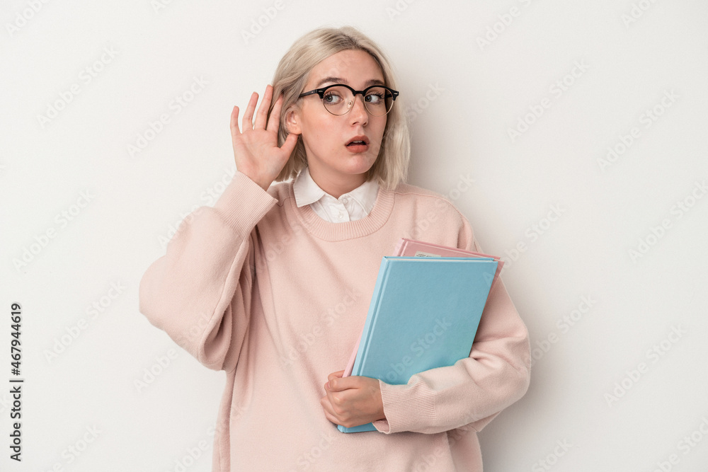 Young caucasian student woman holding books isolated on white background trying to listening a gossip. Young caucasian student woman holding books isolated on white background trying to listening a gossip.