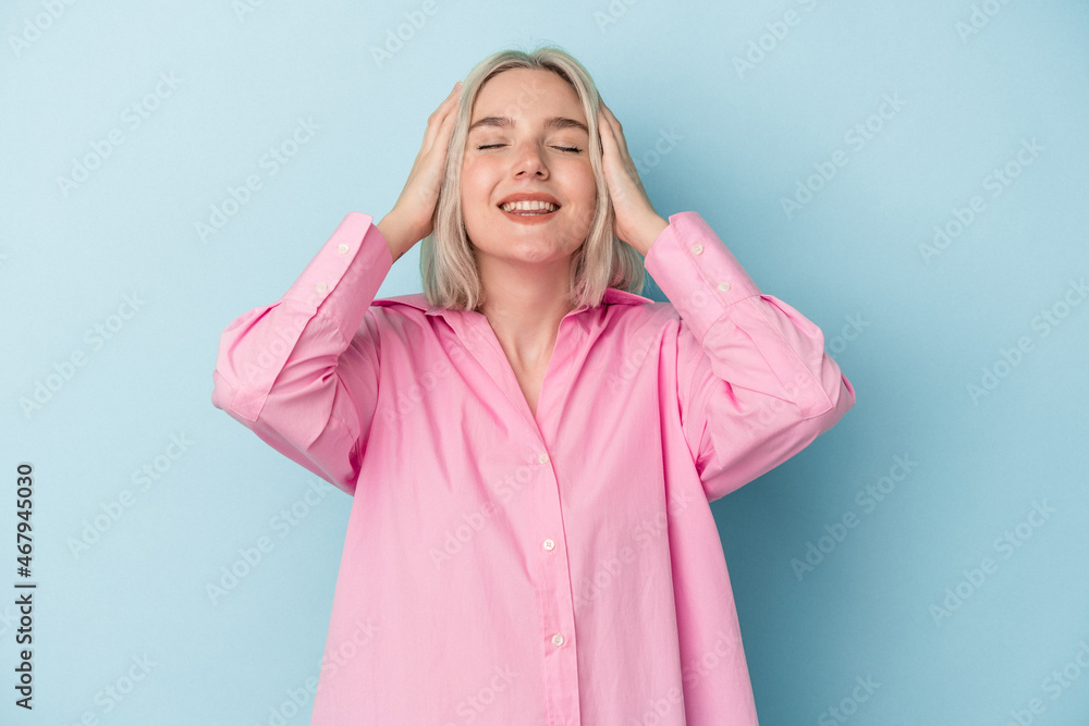 Young caucasian woman isolated on blue background laughs joyfully keeping hands on head. Happiness concept. Young caucasian woman isolated on blue background laughs joyfully keeping hands on head. Happiness concept.