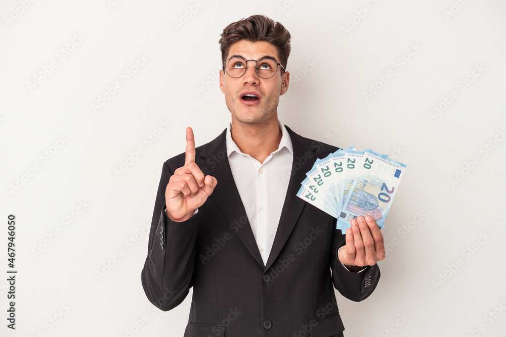 Young business caucasian man holding banknotes isolated on white background pointing upside with opened mouth. Young business caucasian man holding banknotes isolated on white background pointing upside with opened mouth.