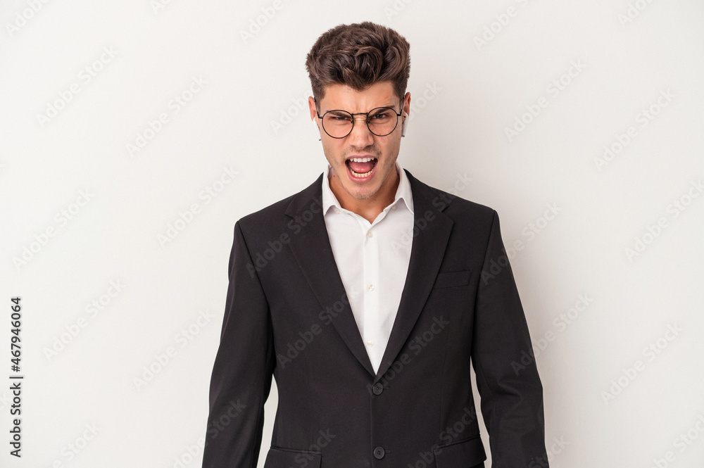 Young business caucasian man wearing headphones isolated on white background screaming very angry and aggressive. Young business caucasian man wearing headphones isolated on white background screaming very angry and aggressive.