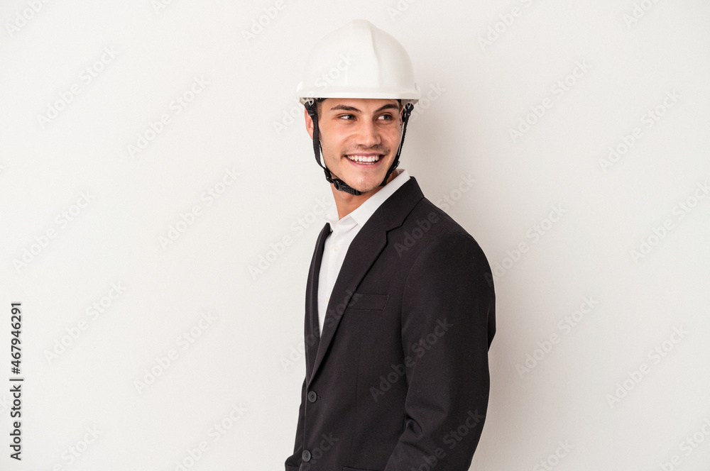 Young architect caucasian man isolated on white background looks aside smiling, cheerful and pleasant.
