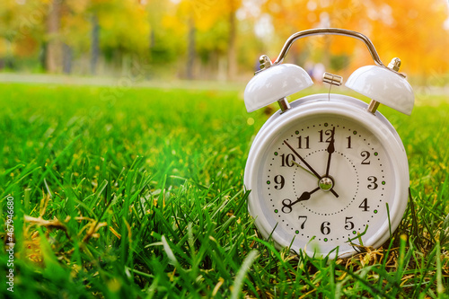 the white clock shows eight o'clock in the morning. The clock stands on the grass, against a background of yellow foliage. Autumn mood. Good morning . Relaxation time, enjoy a wonderful morning.
