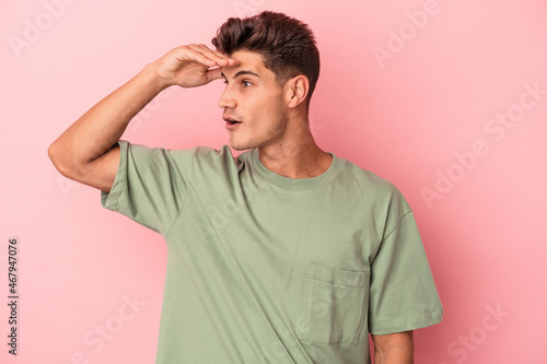 Young caucasian man isolated on pink background looking far away keeping hand on forehead. © Asier