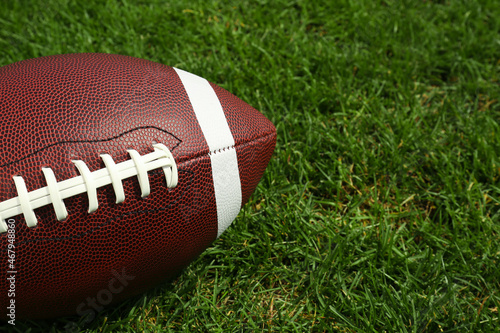 American football ball on green grass, closeup. Space for text