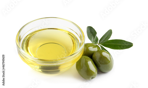 Glass bowl of oil, ripe olives and green leaves on white background