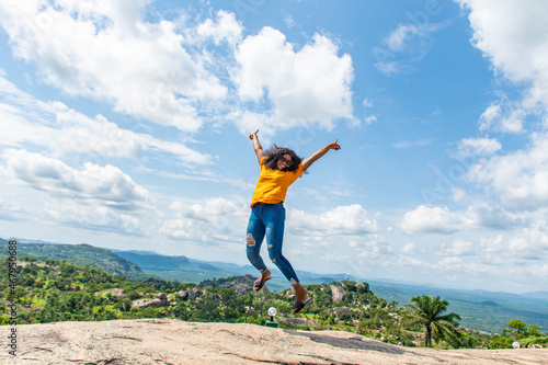 black lady jumps with excitement, in front of a beautiful landscape