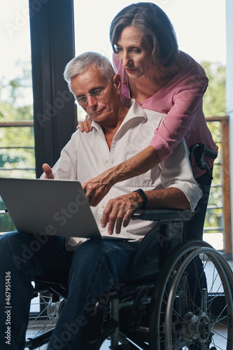 Aging female pointing at laptop screen of wheelchair user