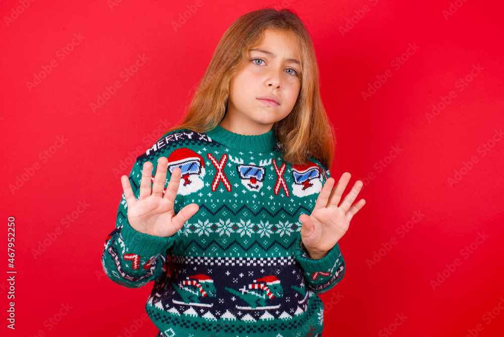 Afraid brunette kid girl in knitted sweater Christmas over red background , makes terrified expression and stop gesture with both hands saying: Stay there. Panic concept. Afraid brunette kid girl in knitted sweater Christmas over red background , makes terrified expression and stop gesture with both hands saying: Stay there. Panic concept.