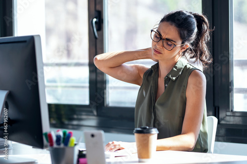 Tired business woman with neck pain looking uncomfortable while working with computer in the office.
