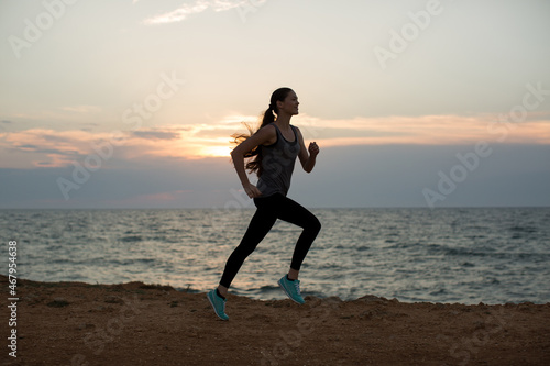 Silhouette of a young girl running along the beach of the sea during an amazing sunset.