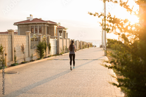Young sporty woman running in the city at sunset. Rear view sporty girl working on the waterfront © Artem Zakharov