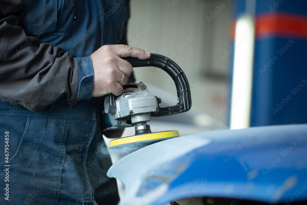 A man who sanding with a grinder and prepares the paint for the car in a car service. Repairman fix car paint A man who sanding with a grinder and prepares the paint for the car in a car service. Repairman fix car paint