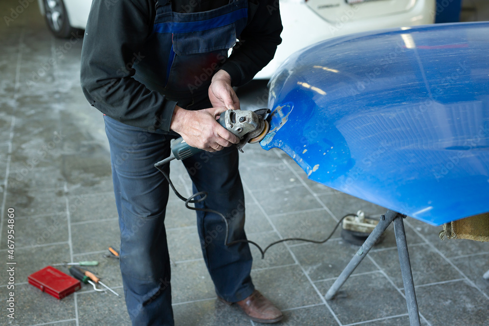 A man who sanding with a grinder and prepares the paint for the car in a car service. Repairman fix car paint A man who sanding with a grinder and prepares the paint for the car in a car service. Repairman fix car paint