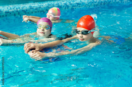 Group of boys and girls train and learn to swim in the pool with an instructor. Development of children's sports. © Artem Zakharov