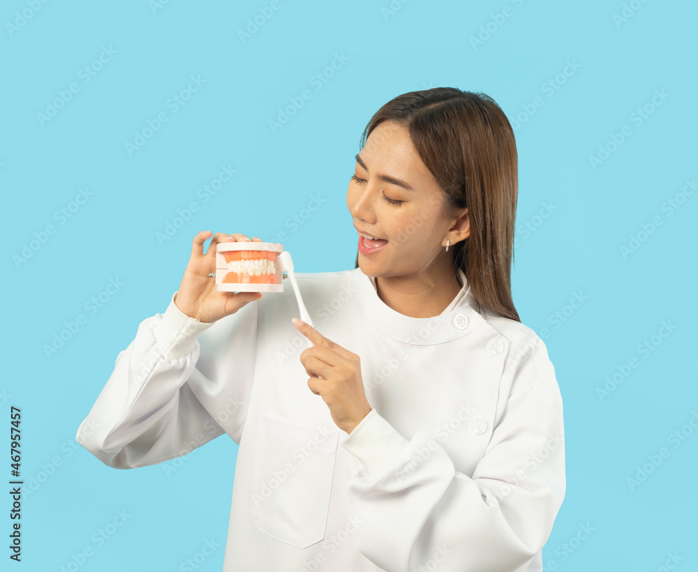 Portrait of happy Asian dentist woman, people smiling, brushing her teeth at hospital clinic. Doctor isolated on blue. Dentistry. Medical and dental health. Portrait of happy Asian dentist woman, people smiling, brushing her teeth at hospital clinic. Doctor isolated on blue. Dentistry. Medical and dental health.