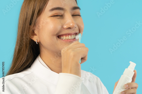 Portrait of happy Asian dentist woman, people smiling, brushing her teeth at hospital clinic. Doctor isolated on blue. Dentistry. Medical and dental health.