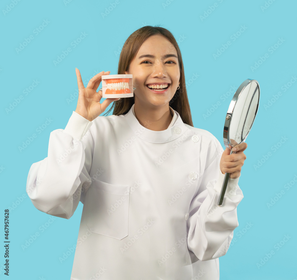 Portrait of happy Asian dentist woman, people smiling, holding denture teeth at hospital clinic. Doctor isolated on blue. Dentistry. Medical and dental health.