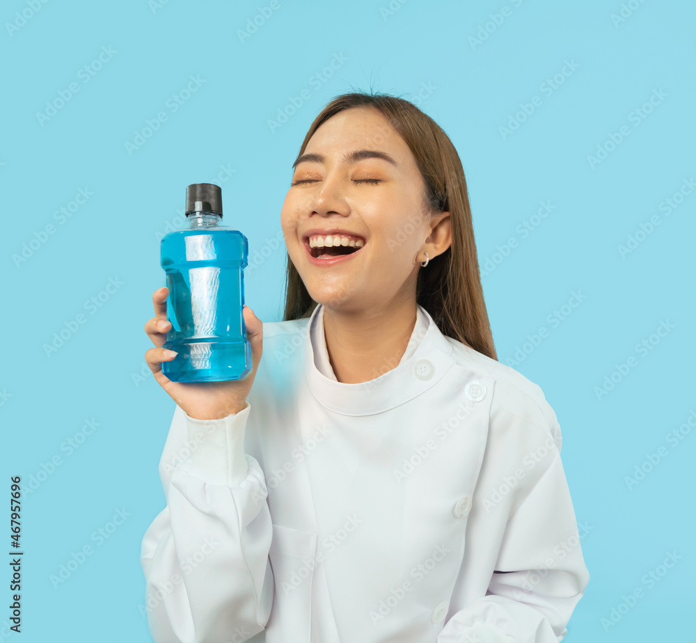 Portrait of happy Asian dentist woman, people smiling, holding mouthwash for teeth at hospital clinic. Doctor isolated on blue. Dentistry. Medical and dental health. Portrait of happy Asian dentist woman, people smiling, holding mouthwash for teeth at hospital clinic. Doctor isolated on blue. Dentistry. Medical and dental health.