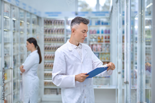 Man in white coat with folder in pharmacy
