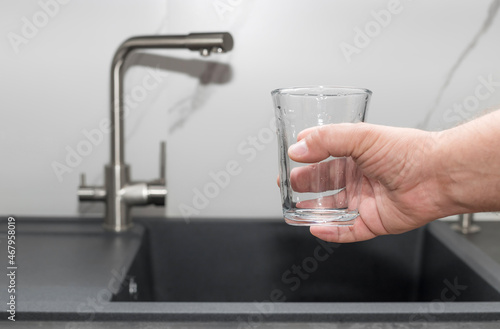 Man ready to pouring filtered water into glass on blurred kitchen background. clean water and healthy life concept. selective focus