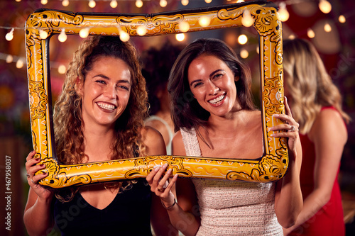 Female Friends Having Fun Posing With Photo Booth Photo Frame At Party In Bar