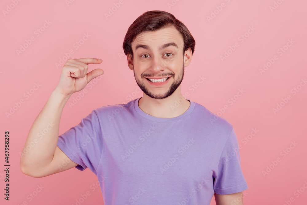 Photo of young man happy positive smile show tiny small size measures with fingers isolated over pink color background Photo of young man happy positive smile show tiny small size measures with fingers isolated over pink color background