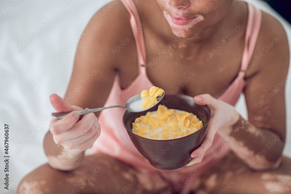 A dark-skinned woman eating cereals while sitting on bed A dark-skinned woman eating cereals while sitting on bed