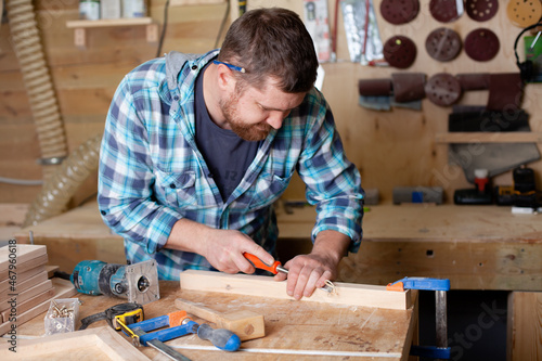  A bearded carpenter in a plaid shirt works a workshop. Wood. Ecological compatibility. Lifestyle.