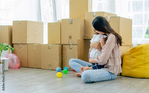 Mother, Little cute Caucasian girl with curly hair sitting on floor in living room, playing toys together with fun, warm hug with love, happiness in house with aper carton boxes for moving new home.
