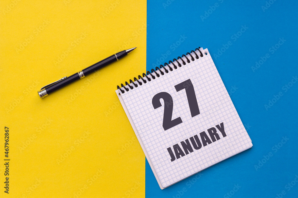 January 27th. Day 27 of month. Calendar date. Notebook with a spiral and pen lies on a yellow-blue background