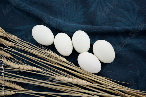 White eggs with dry wheat stems flat lay on blue charade and gray gunsmoke colored organic crumpled texture tea towel, napkin, fabric abstract background.
