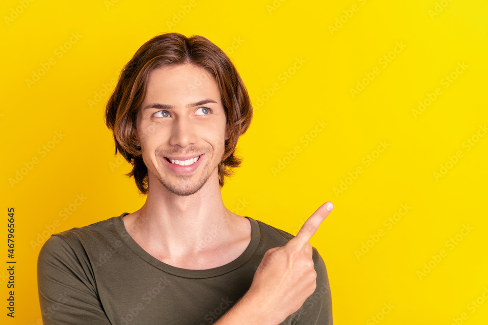 Photo of young guy happy positive smile look indicate finger empty space ads select direct isolated over yellow color background Photo of young guy happy positive smile look indicate finger empty space ads select direct isolated over yellow color background